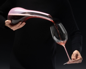 A RIEDEL Fatto A Mano Cabernet/Merlot glass in pink filled with red wine on a white background. 