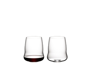 Two SL RIEDEL Stemless Wings Cabernet/Merlot glasses on a transparent background. The SL RIEDEL Stemless Wings Cabernet/Merlot glass on the left side is filled with red wine, the other one is unfilled. 