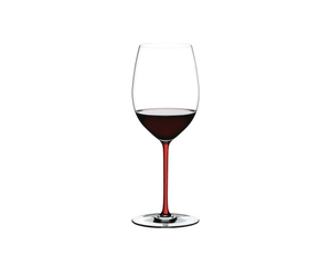 A RIEDEL Fatto A Mano Cabernet/Merlot glass in red filled with red wine on a transparent background. 