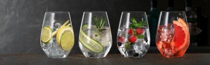 Bicchieri da Gin e Tonic SPIEGELAU su una credenza di legno, ciascuno riempito con un diverso Gin Cocktail.<br/>