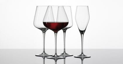 La serie di bicchieri di cristallo ibridi SPIEGELAU mostra un bicchiere di Borgogna pieno di vino rosso e un bicchiere di Bordeaux vuoto, un bicchiere di vino rosso e un bicchiere di champagne.<br/>