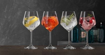 Quattro bicchieri SPIEGELAU Gin and Tonic su un tavolo di legno, ciascuno riempito con un diverso cocktail a base di gin.<br/>