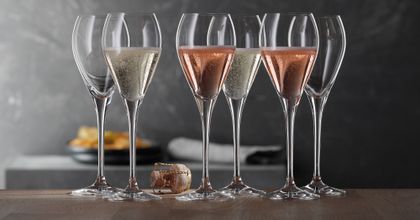 A group of SPIEGELAU Party Champagne glasses. Two of them filled with rosé Champagne, two with regular Champagne and two are empty. There is a cork on the table.<br/>