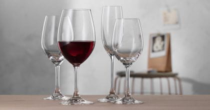 Quattro bicchieri della serie SPIEGELAU Festival. Il bicchiere Bordeaux in primo piano è riempito di vino rosso. Accanto e dietro di esso si trovano un bicchiere da vino bianco vuoto, un bicchiere da degustazione e un flute da Champagne.<br/>
