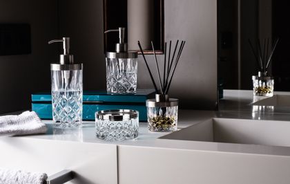 The NACHTMANN Spa Noblesse series on a bathroom sink in front of a mirror. The scent diffuser is filled with fragrance and black sticks. The small and the tall soap dispenser are filled with clear liquid. The storage jar is empty.<br/>