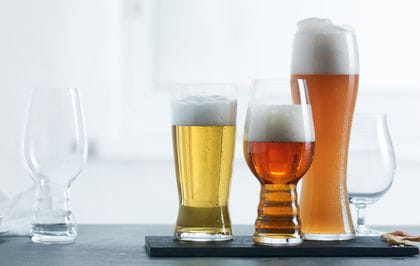 The Spiegelau Craft Beer IPA glass is positioned on the left of the image unfilled with the Spiegelau Beer Classics Tasting Set positioned on the right side of the image filled with their style-specific beer.