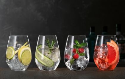 SPIEGELAU Gin und Tonic Gläser auf einem hölzernen Sideboard, jedes davon gefüllt mit einem anderen Gin Cocktail.<br/>