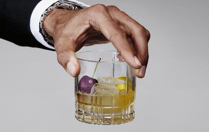 A man's hand holding the Spiegelau Perfect Serve Collection S.O.F glass filled with a Whisky Sour cocktail.