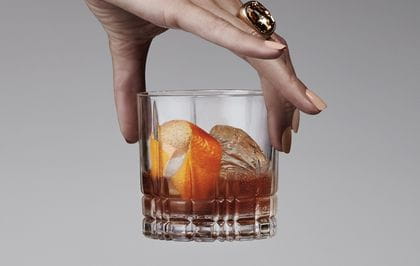 A lady's hand holding a Spiegelau Perfect Serve Collection S.O.F glass filled with an Old Fashioned cocktail.