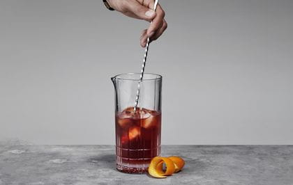 A hand holding a bar spoon, stirring a Negroni cocktail in the Spiegelau Perfect Serve Collection Large Mixing glass.