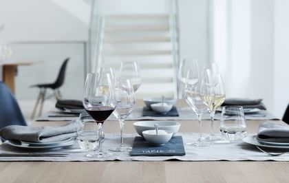 A laid table with three SPIEGELAU glasses at each of the places. On the left place, a with red wine filled Authentis Burgundy glass, an empty white wine glass and a with water filled Authentis Casual tumbler. On the right the Bordeaux glass is empty but the white wine glass is filled.<br/>