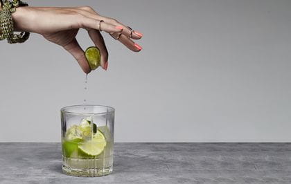 A lady's hand squeezing a lime into the Spiegelau Perfect Serve DOF glass filled with a Capirinha cocktail.