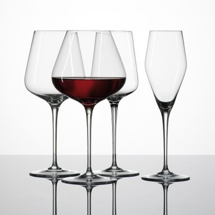 La serie di bicchieri di cristallo ibridi SPIEGELAU mostra un bicchiere di Borgogna pieno di vino rosso e un bicchiere di Bordeaux vuoto, un bicchiere di vino rosso e un bicchiere di champagne.<br/>
