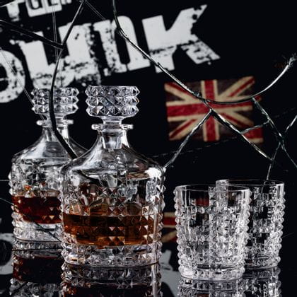 The with whisky filled NACHTMANN Punk decanter and two Punk whisky tumblers on a black table in front of a broken mirror with the written word punk and a junion jack in this mirror.<br/>