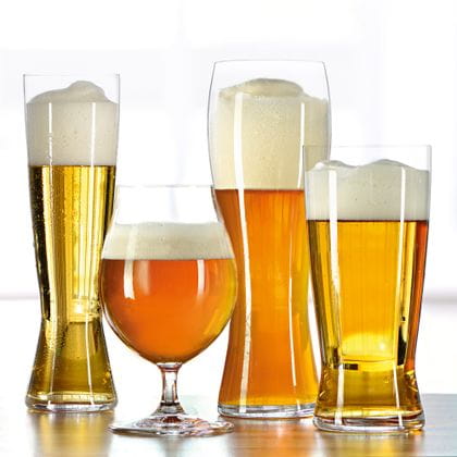 Die vier SPIEGELAU Beer Classics Gläser in einer Reihe, Pilsner, Biertulpe, das Hefeweizenglas und Lager. Gefüllt mit verschiedenen Bieren stehen auf einem Holztisch mit einem hellen Hintergrund. <br/>