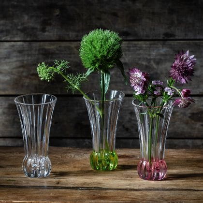 Kleine NACHTMANN-Vasen SPRING auf einem Holztisch. Eine hat einen limonenfarbenen Boden und grüne Blumen darin, die andere einen roséfarbenen Boden und lila Blumen darin.<br/>