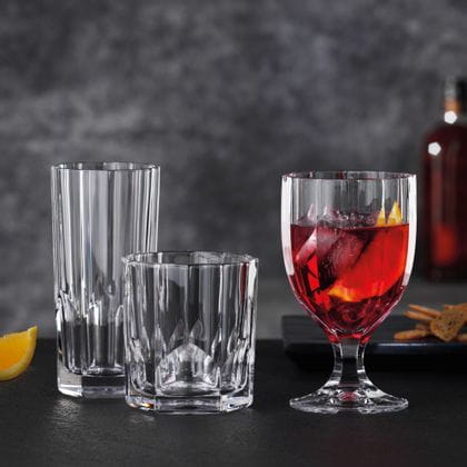Die NACHTMANN-Serie Aspen auf einem schwarzen Tisch. Der Kelch zur Rechten ist mit einem roten Cocktail, Eiswürfeln und einer Orangenscheibe gefüllt. Der Becher und das Longdrinkglas zur Linken sind leer.<br/>