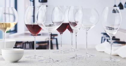 The SPIEGELAU Novo series on a white sideboard. Three of eight glasses are filled with red wine, one with white wine, next to them are three stacked bowls. The rest of the glasses are empty.<br/>