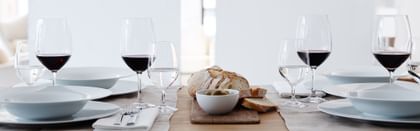The filled SPIEGELAU Vino Grande Bordeaux glass and Mineral Water Glass on a laid table. On the plates there are matching soup plates and besides them is cutlery and bread.<br/>