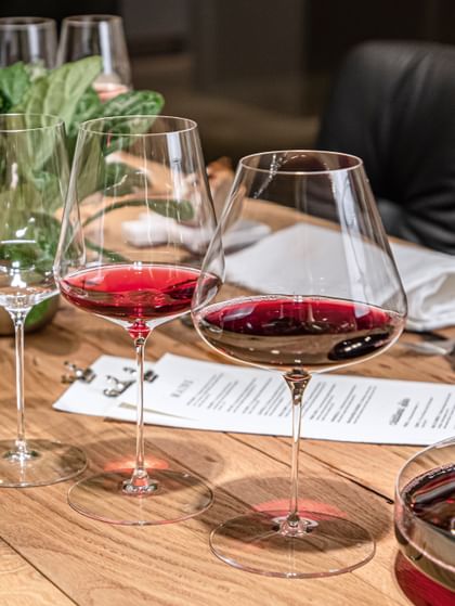The with red wine filled SPIEGELAU Definition Burgundy glass and the Bordeaux glass on a wooden table with an empty Universal glass in the background.<br/>