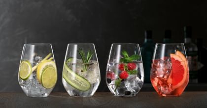 SPIEGELAU Gin und Tonic Gläser auf einem hölzernen Sideboard, jedes davon gefüllt mit einem anderen Gin Cocktail.<br/>