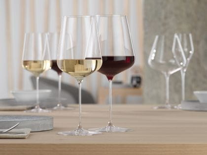 A SPIEGELAU Definition Bordeaux glass filled with red wine and a SPIEGELAU Definition white wine glass filled with white wine on a table. In the background are the same filled wine glasses again.<br/>