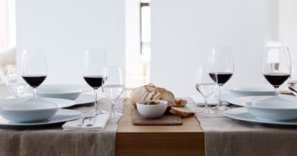 The filled SPIEGELAU Vino Grande Bordeaux glass and Mineral Water Glass on a laid table. On the plates there are matching soup plates and besides them is cutlery and bread.<br/>