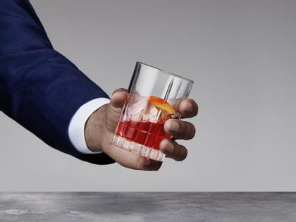 A man's hand holding a Spiegelau Perfect Serve Collection Small Long Drink glass filled with an Americano cocktail.