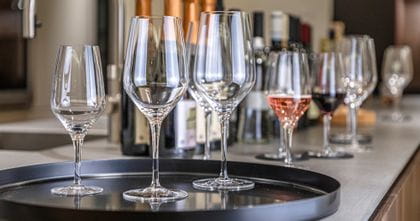 Les trois tailles de la série de verres SPIEGELAU Allround sur un plateau de service. À l'arrière-plan, des bouteilles de champagne.<br/>
