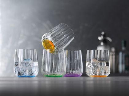 The SPIEGELAU Liefestyle cups in the different colours ocean, leaf, sun and lilac stand in a row. The cup in the colour ocean and sun is filled with water and ice cubes.<br/>