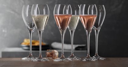 A group of SPIEGELAU Party Champagne glasses. Two of them filled with rosé Champagne, two with regular Champagne and two are empty. There is a cork on the table.<br/>