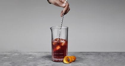 A hand holding a bar spoon, stirring a Negroni cocktail in the Spiegelau Perfect Serve Collection Large Mixing glass.