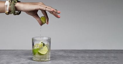 A lady's hand squeezing a lime into the Spiegelau Perfect Serve DOF glass filled with a Capirinha cocktail.