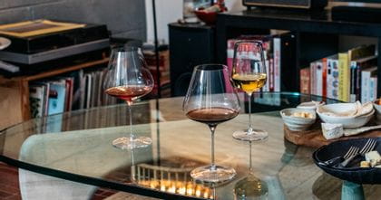 Lifestyle image of two Spiegelau Definition Burgundy glasses and one Spiegelau Definition Universal glass on a glass coffee table filled with wine. In the background is a book shelf filled with books.