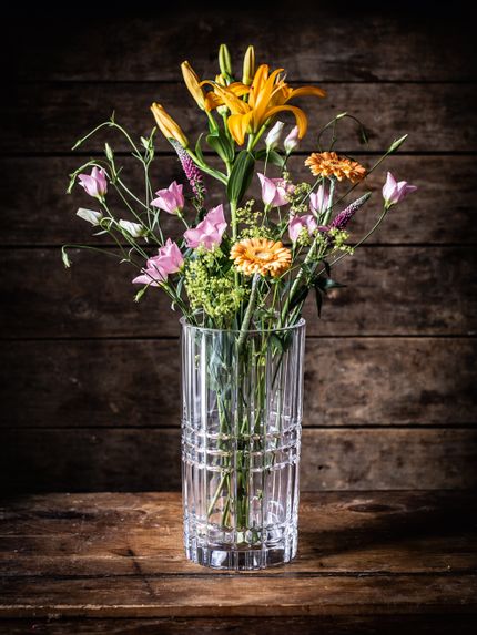 Il vaso quadrato NACHTMANN, pieno di fiori arancioni e rosa, su una credenza in legno scuro.<br/>