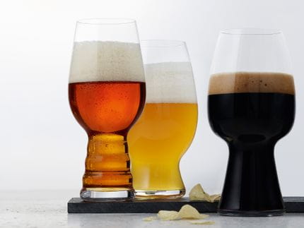The with beer filled SPIEGELAU Craft Beer Glasses. The IPA glass and the American Wheat Beer glass are standing on a slate plate decorated with some potato chips and the Stout glass is standing next to them.<br/>
