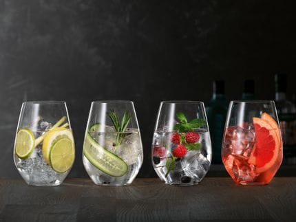 Bicchieri da Gin e Tonic SPIEGELAU su una credenza di legno, ciascuno riempito con un diverso Gin Cocktail.<br/>