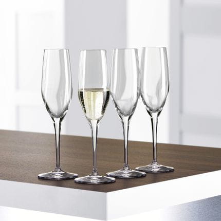 Cuatro copas de champán SPIEGELAU Authentis sobre una mesa, una de ellas llena de vino espumoso.<br/>