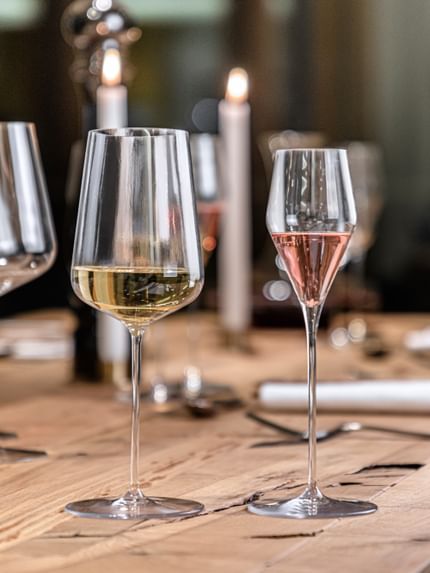 The SPIEGELAU Definition white wine glass filled with white wine and the digestive glass filled with a pink aperitif standing on a wooden table.<br/>