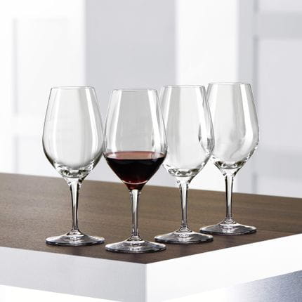 Cuatro copas de cata SPIEGELAU Authentis sobre una mesa, una de ellas llena de vino tinto.<br/>
