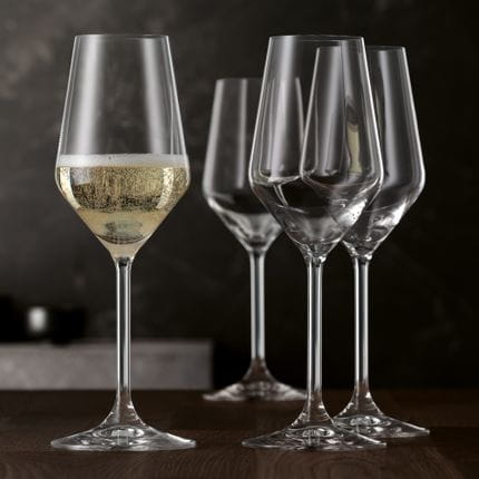 Quatre coupes à champagne de style SPIEGELAU sur une table en bois. Une coupe est remplie de vin mousseux.<br/>