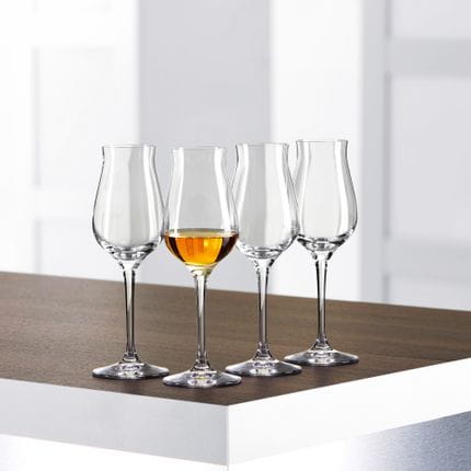 Quattro bicchieri SPIEGELAU Authentis Digestive su un tavolo, uno dei quali è riempito con un liquore marrone dorato.<br/>
