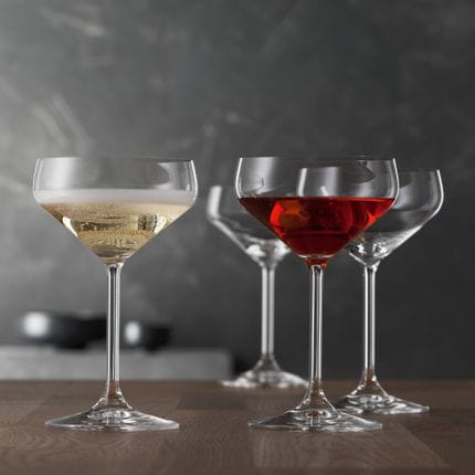 Quatre verres à coupette de style SPIEGELAU. Un verre au premier plan est rempli de champagne, un autre d'une boisson rouge.<br/>