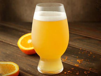SPIEGELAU Craft Beer American Wheat Beer glass filled with beer on a wooden bench surrounded by cut oranges.