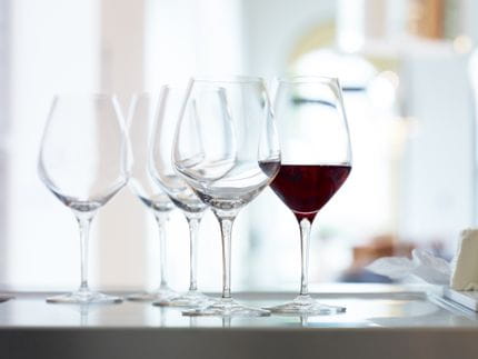 Eine gemischte Gruppe von SPIEGELAU Bordeaux- und Burgundergläsern auf einer Anrichte. Das Bordeaux-Glas ist mit Rotwein gefüllt.<br/>