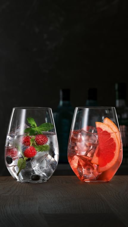 Bicchieri da Gin e Tonic SPIEGELAU su una credenza di legno, ciascuno riempito con un diverso Gin Cocktail.<br/>