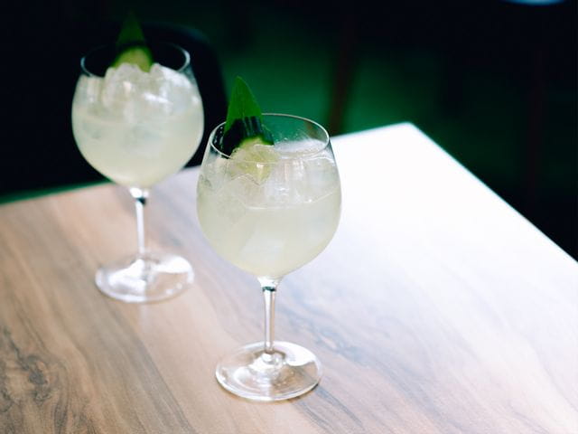 Two SPIEGELAU Gin & Tonic glasses filled with G&T on a wooden benchtop.