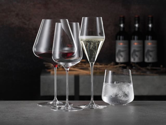 Das mit Rotwein gefüllte SPIEGELAU Definition Burgunderglas, das gefüllte Champagnerglas, das leere Weißweinglas und der mit Wasser und Eiswürfeln gefüllte Trinkbecher.<br/>