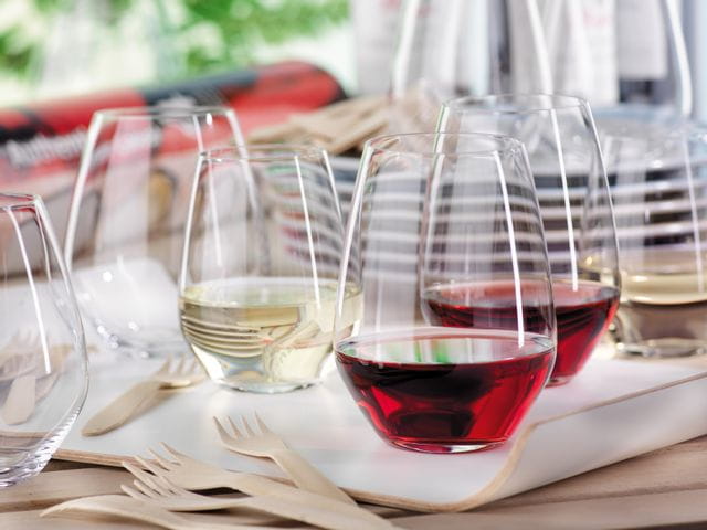 SPIEGELAU Authentis Bicchieri casual su un vassoio di servizio su un tavolo all'aperto. Due dei bicchieri senza stelo sono riempiti di vino rosso, uno di vino bianco. In primo piano ci sono forchette di legno e sullo sfondo una pila di piatti e altri bicchieri.<br/>