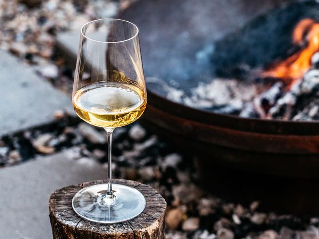 Spiegelau Definition Universal glass filled with white wine standing on a wooden log next to a fire.
